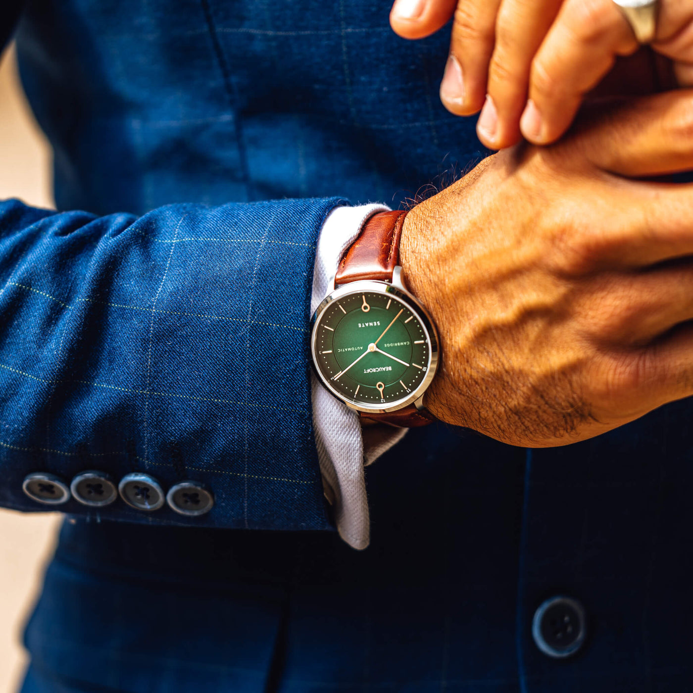 The wrist of a man wearing the Eden Green Beaucroft Senate watch with a blue suit