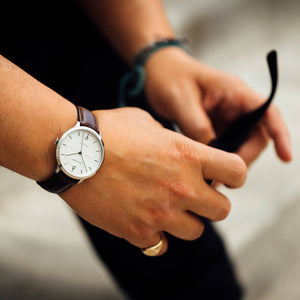 The wrist of a man wearing the white Beaucroft Senate watch with Cambridge blue leather strap with sunglasses 